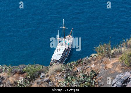 Santorin, Griechenland - 8. Oktober 2019: Ein ruhiges Segelboot vor Santorinis zerklüfteter Küste ankert. Stockfoto