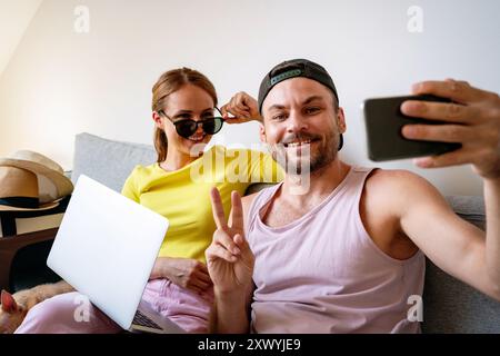 Das junge Paar sitzt zu Hause auf der Couch, hat Spaß und macht Selfie mit dem Handy. Stockfoto