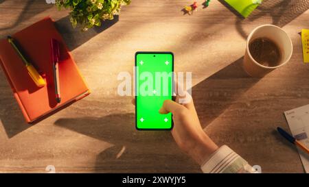 Business Manager scrollen durch Apps auf dem Smartphone mit Green Screen Chromakey Mock Up Display in einem kreativen Arbeitsplatz. Fotovorlage mit isoliertem Platzhalter für digitales Marketing – Demo Stockfoto