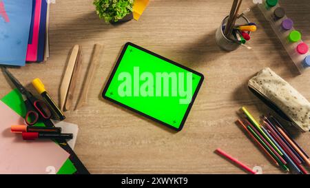 Top-Down-Ansicht eines Tablet-Computers mit Mock-Up Green Screen Display. Digitales Gerät, das horizontal auf einem Tisch in einem Künstlerstudio liegt. Vorlage für kreative Online-Tutorials oder soziale Medien Stockfoto
