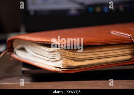 Braunes Ledernotizbuch liegt auf schwarzem Laptop im Büro, im Arbeitsbuch, im Tagebuch für Notizen Stockfoto