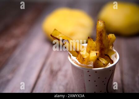 Pommes frites in einer kleinen Tasse. Im Hintergrund kann man noch leicht eine Kartoffel erkennen Stockfoto