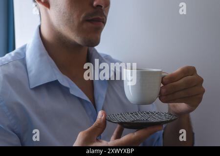 Ein junger Geschäftsmann nimmt an einem Geschäftstreffen Teil, während er an einem normalen Arbeitstag eine Tasse Kaffee in einem blauen Hemd trinkt. Stockfoto