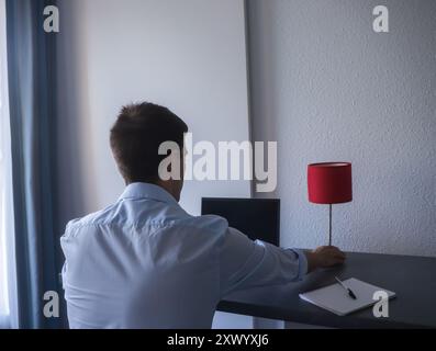 Rückansicht eines jungen Geschäftsmannes, der in seinem Heimbüro arbeitet und ein blaues Hemd an seinem Laptop trägt. Stockfoto