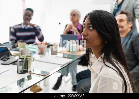 Aufmerksame junge Geschäftsfrau in diversen Teammeetings. Multiethnische und generationenübergreifende Fachkräfte versammelten sich am Tisch. Vielfalt am Arbeitsplatz, Co Stockfoto