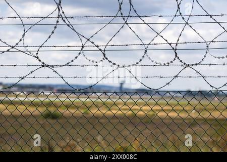 Flughafen Nürnberg Detailaufnahme eines Sicherheitszauns mit Stacheldraht um das Gelände des Albrecht Dürer Airport Nürnberg. Im Hintergrund ist unscharf der Kontrollturm des Flughafens zu erkennen. Der Zaun war in der vergangenen Woche das Ziel einer Sabotageaktion, bei der Aktivisten der Gruppe Letzte Generation den Zaun durchtrennten und sich auf der Landebahn festklebten. Nürnberg Bayern Deutschland *** Nürnberg Flughafen Nahaufnahme eines Sicherheitszauns mit Stacheldraht rund um das Gelände des Albrecht Dürer Flughafens Nürnberg der Flughafenleitturm ist im Hintergrund L unscharf zu sehen Stockfoto