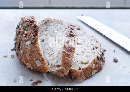 UK Ein Stück frisch gebackenes traditionelles Sauerteigbrot mit mehreren Saaten. Das Brot liegt auf einem Schneidebrett, nachdem es mit einem Brotmesser geschnitten wurde Stockfoto