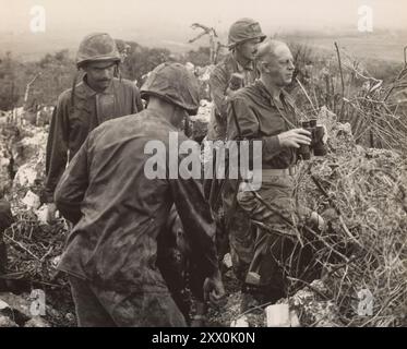 2. Weltkrieg: Schlacht von Tinian. Teil der Kampagne Mariana und Palau Islands des Pacific Theater. 24. Juli bis 1. August 1944 Beobachter an der Front. Von einem Beobachtungsposten auf dem Mount Lasso hält Marinebrigadegeneral Merritt A. Edson (barköpfig), Guadalcanal- und Tarawa-Veteran, seine Truppen im Auge, während sie japanische Positionen auf Tinian stürmen, der neuesten Mariana-Gruppe, die von den Leathernechen erobert wurde. Stockfoto