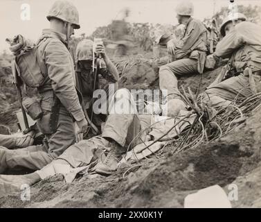 2. Weltkrieg: Schlacht von Iwo Jima (19. Februar bis 26. März 1945). Eine Zigarette und Plasma... Da ihm Marinesoldaten helfen, ein Marinekorpsmann ein verwundetes Marineblut zwischen Motoyama Airstrip Nummer zwei und Purple Beach an D plus Three Day geben, gewinnt der Verletzte ein wenig Freude an einer Zigarette. Jwo Jime, Japan Stockfoto