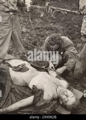 2. Weltkrieg: Schlacht von Cape Gloucester. 26. Dezember 1943 und 16. Januar 1944. Blutplasma für verwundete Marine: PFC. Theodore Rutkowski, 936 Fields St., Hammond, Ind., einer der Marines, die in Cape Gloucester eingefallen sind, erhält Plasma, damit er Blutverlust durch eine Wunde aushalten kann. Der Marinekorpsman, der die Behandlung durchführt, ist PhMl/c Robert B. McGregor, USN, Griffin Road, Littlerock, Kalifornien Stockfoto