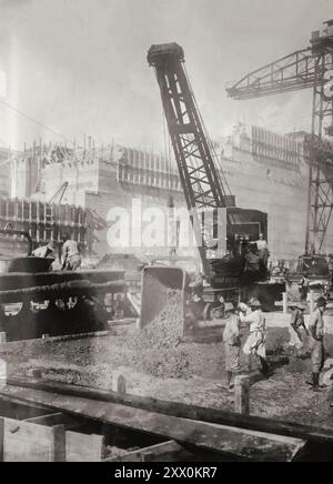 Pedro Miguel verriegelt. Hilfskran, der Beton abwirft, Panamakanal. Die Schleusen des Panamakanals (Spanisch: Esclusas del Canal de Panamá) sind ein Schleusensystem, das Schiffe 85 Fuß (26 Meter) bis zur Haupthöhe des Panamakanals und wieder hinunter bringt. Der ursprüngliche Kanal hatte insgesamt sechs Stufen (drei nach oben, drei nach unten) für die Passage eines Schiffes. Die Gesamtlänge der Schleusenkonstruktionen einschließlich der Zugangswände beträgt mehr als 3 km (1,9 Meilen). Die Schleusen waren eine der größten Bauarbeiten, die jemals durchgeführt wurden, als sie 1914 eröffnet wurden. Stockfoto