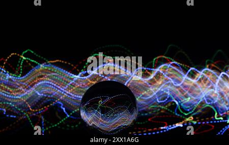 Ein Foto mit langer Belichtung. Lichtmalerei - wirbelnde Wellen von Neonlicht hinter einer Glaskugellinse. Stockfoto