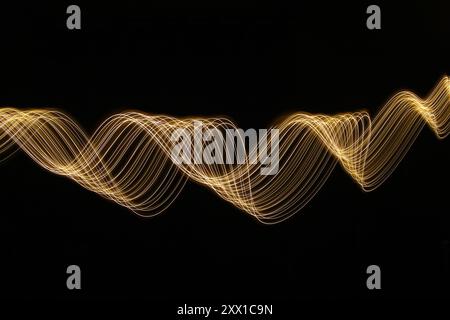Ein Foto mit langer Belichtung. Lichtmalerei Fotografie - wirbelnde Wellen aus Neongelbgold auf schwarzem Hintergrund Stockfoto