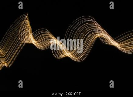 Ein Foto mit langer Belichtung. Lichtmalerei Fotografie - wirbelnde Wellen aus Neongelbgold auf schwarzem Hintergrund Stockfoto