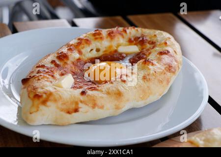 Traditionelles georgianisches Brot mit Käse, Butter und Ei, bekannt als Adjaruli Khachapuri Teller, in Nahaufnahme auf dem Tisch Stockfoto