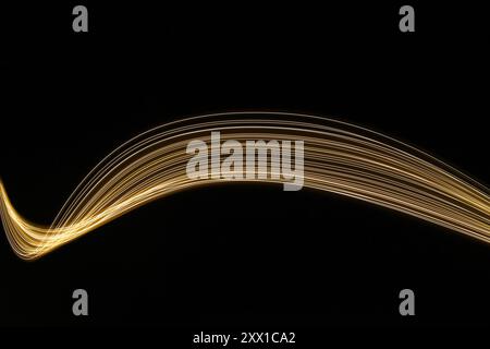 Ein Foto mit langer Belichtung. Lichtmalerei Fotografie - wirbelnde Wellen aus Neongelbgold auf schwarzem Hintergrund Stockfoto