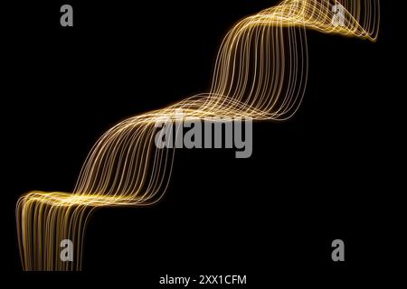 Ein Foto mit langer Belichtung. Lichtmalerei Fotografie - wirbelnde Wellen aus Neongelbgold auf schwarzem Hintergrund Stockfoto