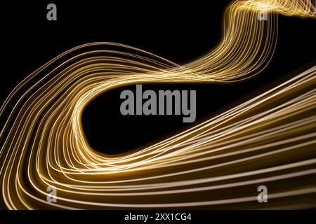 Ein Foto mit langer Belichtung. Lichtmalerei Fotografie - wirbelnde Wellen aus Neongelbgold auf schwarzem Hintergrund Stockfoto