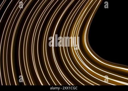 Ein Foto mit langer Belichtung. Lichtmalerei Fotografie - wirbelnde Wellen aus Neongelbgold auf schwarzem Hintergrund Stockfoto