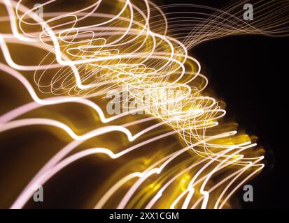 Ein Foto mit langer Belichtung. Lichtmalerei Fotografie - wirbelnde Wellen aus Neongelbgold auf schwarzem Hintergrund Stockfoto