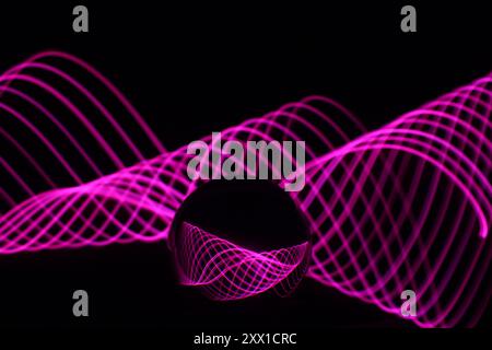 Ein Foto mit langer Belichtung. Lichtmalerei - wirbelnde Wellen von Neonlicht hinter einer Glaskugellinse. Stockfoto
