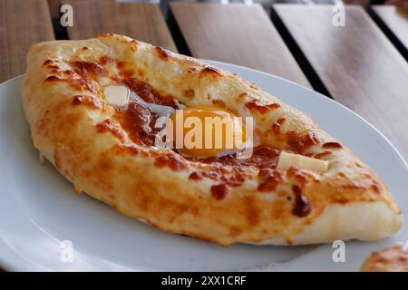 Traditionelles georgianisches Brot mit Käse, Butter, Ei, bekannt als Adjaruli Khachapuri Teller in Nahaufnahme auf einem Tisch Stockfoto