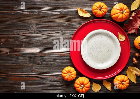 Leere rote und weiße Teller auf dunklem Holzhintergrund im Herbstdekor, Blick von oben. Stockfoto