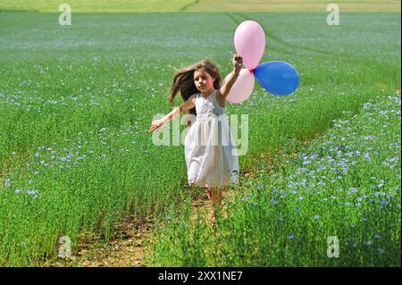 Kleines Mädchen in weiß gekleidet, das mit Ballons auf einem Blumenflachsfeld spielt, Centre-Val de Loire Region, Frankreich, Europa Stockfoto