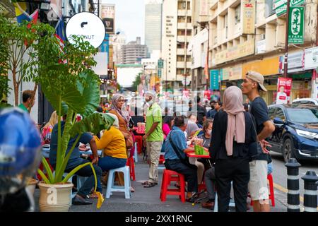 Kleine lokale asiatische Straßenrestaurants mit Plastikstühlen und Tischen auf dem Bürgersteig entlang der Straße. Kuala Lumpur, Malaysia - 11.15.2022 Stockfoto