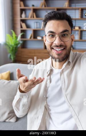 Vertikale Nahaufnahme eines jungen Indianers in lässiger Kleidung, der zu Hause ist, ein Video aufnimmt, online mit der Kamera spricht und mit den Händen Gesten macht. Stockfoto
