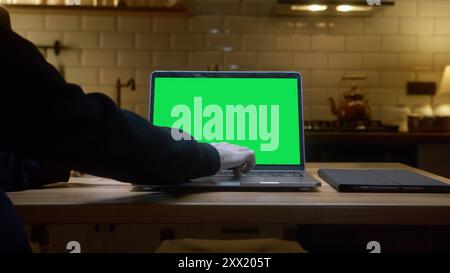 Ein Laptop mit grünem Bildschirm auf einer Küchenarbeitsplatte, weißer Kaffeetasse. Eine Person mit Laptop in der modernen Küche. Stockfoto
