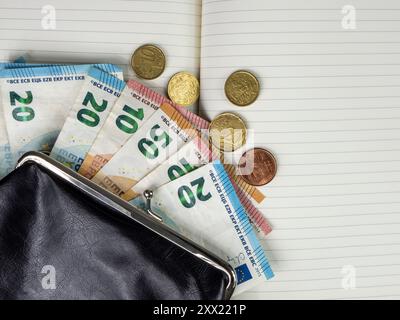 Draufsicht der Geldbörse mit Euro-Geld auf dem geöffneten Notizblock. Mehrere Euro-Münzen sichtbar. Stockfoto