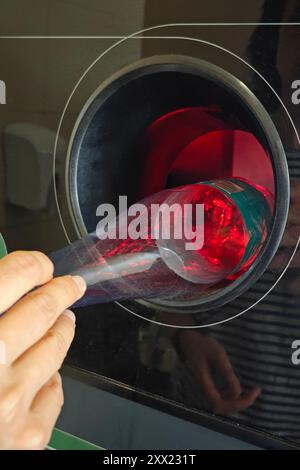 Umkehrautomat. Frau hat leere Plastikflasche in die Maschine gesteckt. Umkehrautomat für Erstattung und Recycling von Getränkedosen aus Metall, Kunststoff und Stockfoto