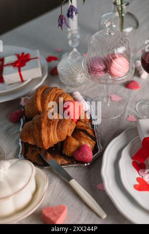 Blick von oben auf einen eleganten romantischen Tisch für zwei Personen mit Geschenken, Croissants, Makronen, süßen Leckereien und herzförmigen Dekorationen Stockfoto