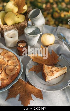 Nahaufnahme eines Apfelkuchen und Tee mit einem Korb Äpfel auf einem herbstlichen Gartentisch in der Sonne Stockfoto