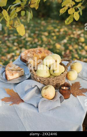 Nahaufnahme eines Apfelkuchen und eines Korbes frischer Äpfel auf einem herbstlichen Gartentisch in der Sonne Stockfoto
