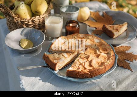 Nahaufnahme eines Apfelkuchen und Tee mit einem Korb Äpfel auf einem herbstlichen Gartentisch in der Sonne Stockfoto