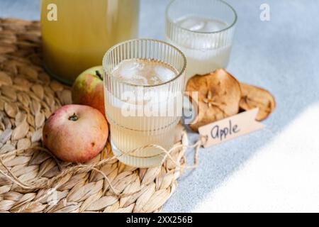 Kanne und zwei Gläser frischen Apfelsaft auf einer Tischmatte mit frischen Äpfeln, getrockneten Apfelscheiben und einem Etikett mit dem Wort Apfel Stockfoto