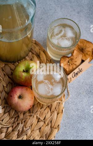 Kanne und zwei Gläser frischen Apfelsaft auf einer Tischmatte mit frischen Äpfeln, getrockneten Apfelscheiben und einem Etikett mit dem Wort Apfel Stockfoto