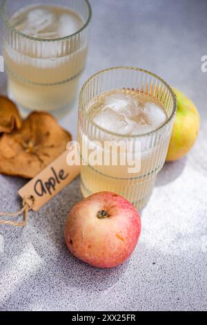 Nahaufnahme von zwei Gläsern frischen Apfelsafts auf einer Tischmatte mit frischen Äpfeln, getrockneten Apfelscheiben und einem Tag mit dem Wort Apfel Stockfoto