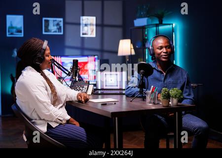 Afroamerikanische Influencer in einem gemütlichen Heimstudio, Kopfhörer an, die ihr Publikum mit einer unterhaltsamen Online-Diskussion begeistern. Ersteller von schwarzen Inhalten, die einen Vlog für Social-Media-Plattformen aufzeichnen Stockfoto