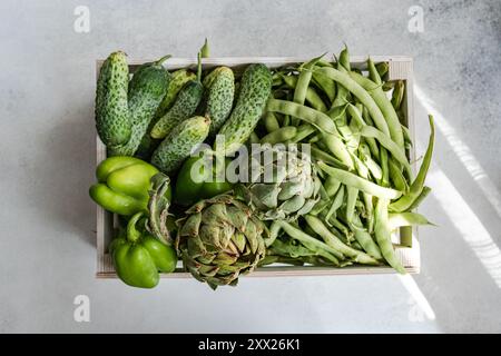 Aus nächster Nähe sehen Sie frische Artischocken, Stufenbohnen, Gurken und grüne Paprika in einer Holzkiste Stockfoto