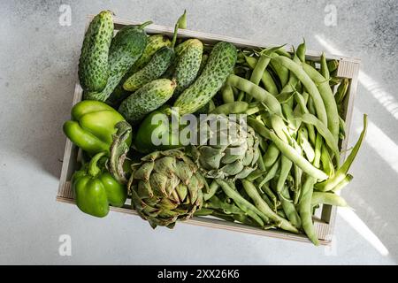 Aus nächster Nähe sehen Sie frische Artischocken, Stufenbohnen, Gurken und grüne Paprika in einer Holzkiste Stockfoto