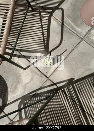 Blick von oben auf ein eiskaltes Matcha Latte Getränk auf dem Boden im Schatten von Gartenstühlen Stockfoto