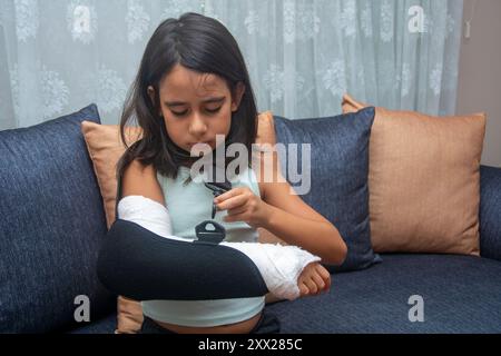 Ein kleines Mädchen mit gebrochenem Arm zieht die Clips ihrer Bandage an Stockfoto