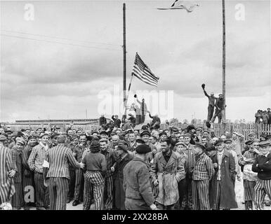 Überlebende, die eine hausgemachte amerikanische Flagge schwenken, begrüßen die Truppen der 7. Armee bei ihrer Ankunft im Konzentrationslager Allach. Allach war ein Unterlager des Dachau-Komplexes und stellte Zwangsarbeit für die nahe gelegenen Industrien bereit. Stockfoto