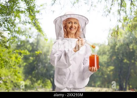 Imker in Uniform, der Honig aus einem Glas probiert und lächelt Stockfoto