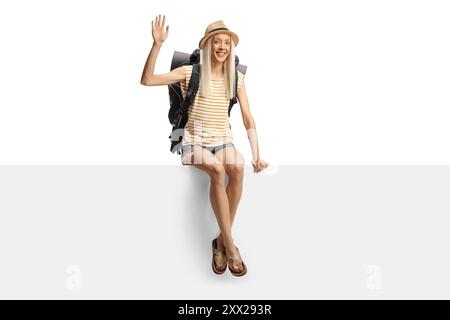 Backpackerin sitzt auf einer leeren Platte und winkt isoliert auf weißem Hintergrund Stockfoto