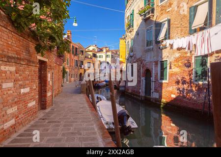 Ein venezianischer Kanal, gesäumt von Ziegelgebäuden, einem kleinen Boot und Wäscherei, die über der Gasse in Venedig, Italien, hängen Stockfoto