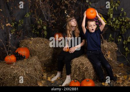 Glückliche Bruder und Schwester an Halloween. Lustige Kinder in Karnevalskostümen drinnen. Fröhliche Kinder spielen mit Kürbissen Stockfoto